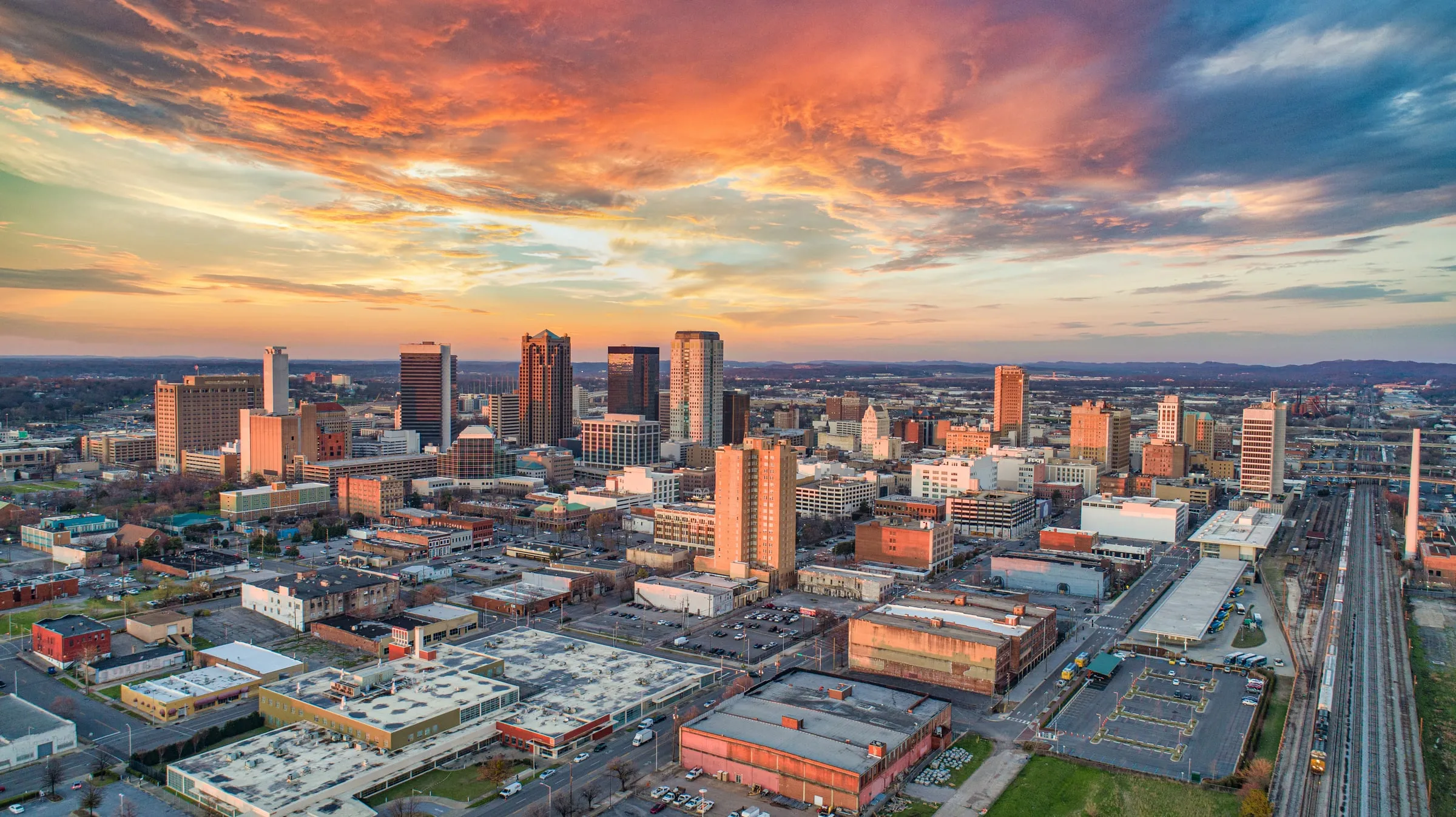 Aerial view of downtown Birmingham, Alabama at sunset, the skyline under orange clouds with the rail yard running along the right